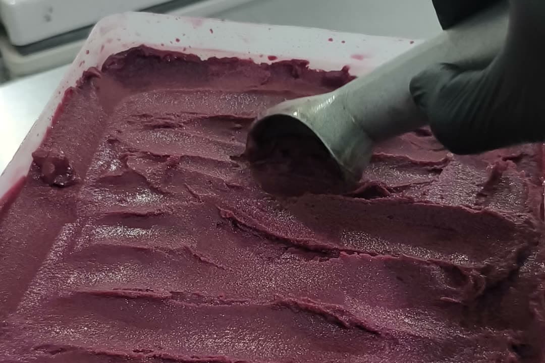Caixa de 10 litros de açaí Algo Mais aberta na fábrica, com a massa espatulada e o boleador em mãos